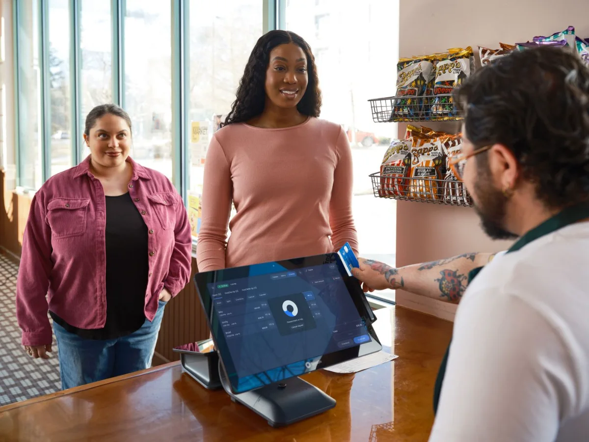 Cajero cobrando con una computadora de punto de venta a clientas en una tienda